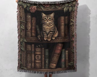 Op de afbeelding: Een geweven tapijtdeken met een bruine tabbykat die op een boekenkast zit vol met antieke boeken. De boekenkast is versierd met wijnstokken en rozen.