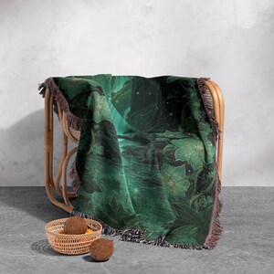 May include: A green and black floral throw blanket draped over a wicker chair. The blanket features a botanical design with large flowers and foliage. The blanket has a fringed edge and is approximately 60 inches by 50 inches.