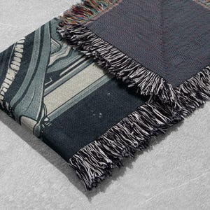 May include: A black and white woven throw blanket with a geometric pattern. The blanket has a fringe border.