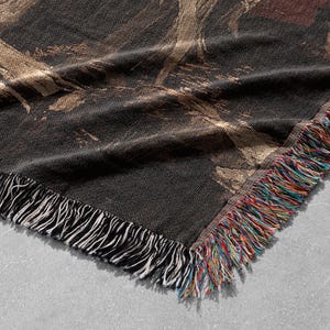 May include: A black and gold woven throw blanket with a fringed edge. The blanket has a textured, abstract design.