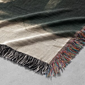 May include: A woven throw blanket with a colorful fringe and a faded abstract design in shades of brown, green, and white.