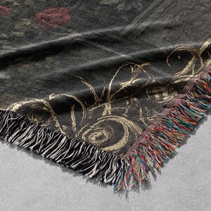 Puede incluir: Una manta tejida de color negro y dorado con un patr&oacute;n floral y bordes con flecos. La manta tiene una superficie texturizada y un brillo sutil.