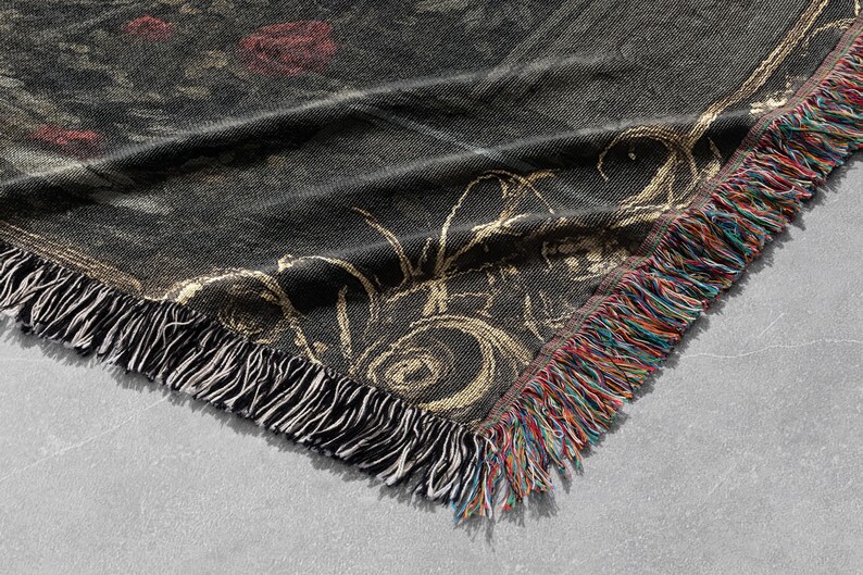 Puede incluir: Una manta tejida de color negro y dorado con un patr&oacute;n floral y bordes con flecos. La manta tiene una superficie texturizada y un brillo sutil.