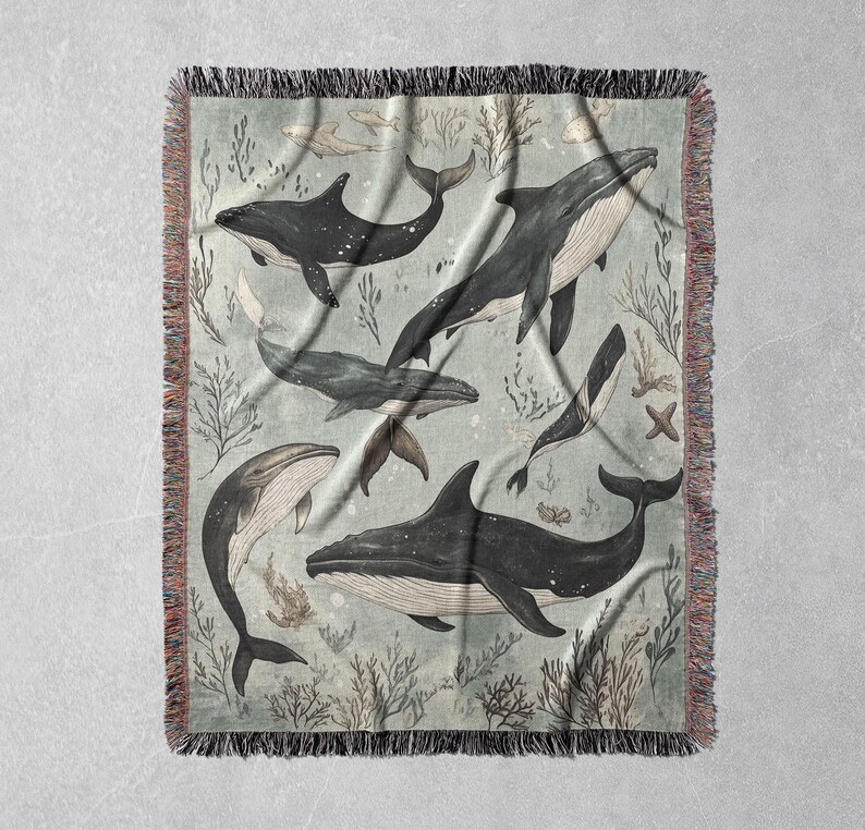 May include: A woven tapestry featuring a blue and white design of whales swimming in a sea of coral and seaweed. The tapestry has a fringed border.