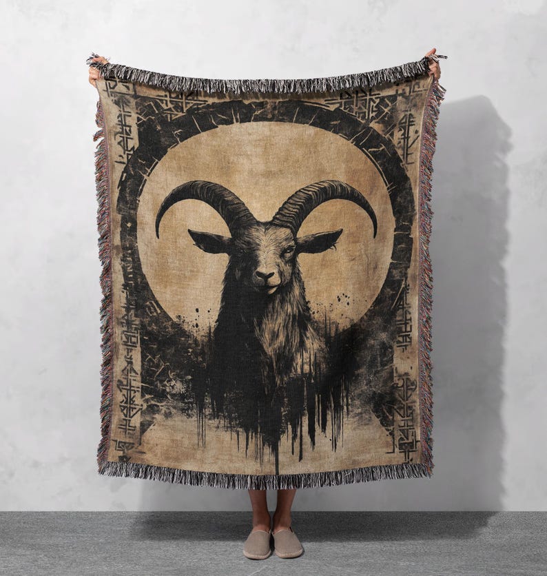 Pu&ograve; includere: Una coperta in tessuto intrecciato con un'illustrazione in bianco e nero di una testa di capra con corna in un cerchio su uno sfondo marrone.
