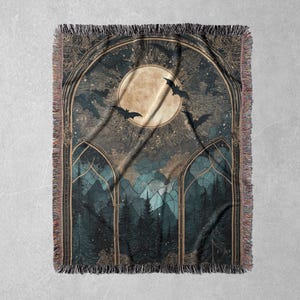 May include: A woven throw blanket featuring a gothic forest scene with a full moon, bats, and a starry sky. The design is framed by arched windows and detailed with fringe edges. The color palette includes shades of blue, brown, and gold.