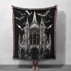 Op de afbeelding: Zwart-wit geweven wandkleed met een gotische kathedraal met vleermuizen die eromheen vliegen.