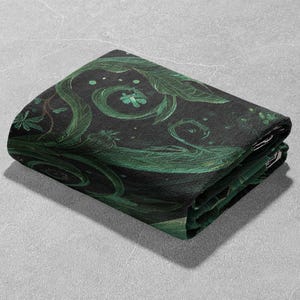 May include: Folded black fabric with a green botanical design featuring swirling vines, leaves, and small floral accents. The fabric is folded neatly, showcasing the detailed pattern and color variations.