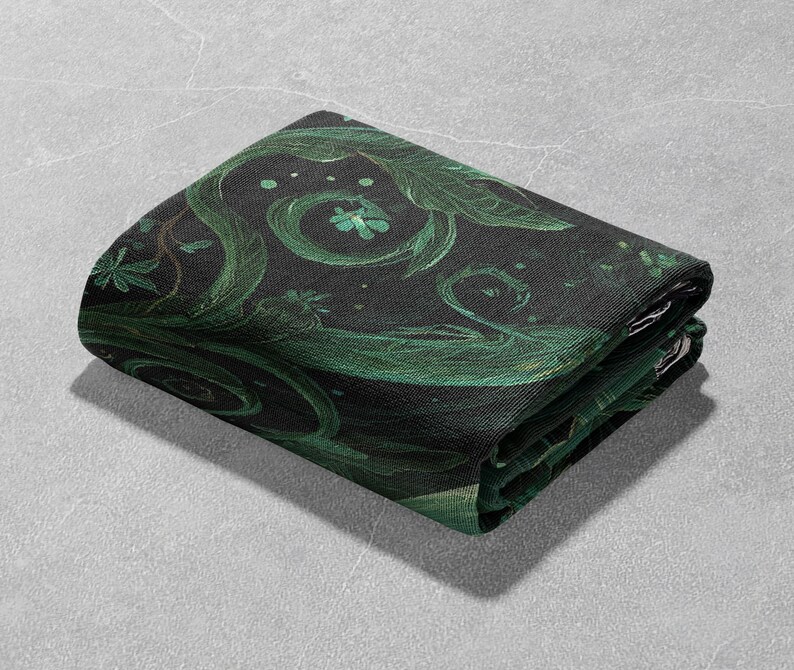 May include: Folded black fabric with a green botanical design featuring swirling vines, leaves, and small floral accents. The fabric is folded neatly, showcasing the detailed pattern and color variations.