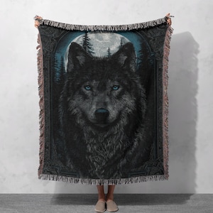 May include: A woven throw blanket with a detailed illustration of a wolf with striking blue eyes. The wolf is set against a backdrop of a full moon and a forest, with decorative borders and fringed edges.