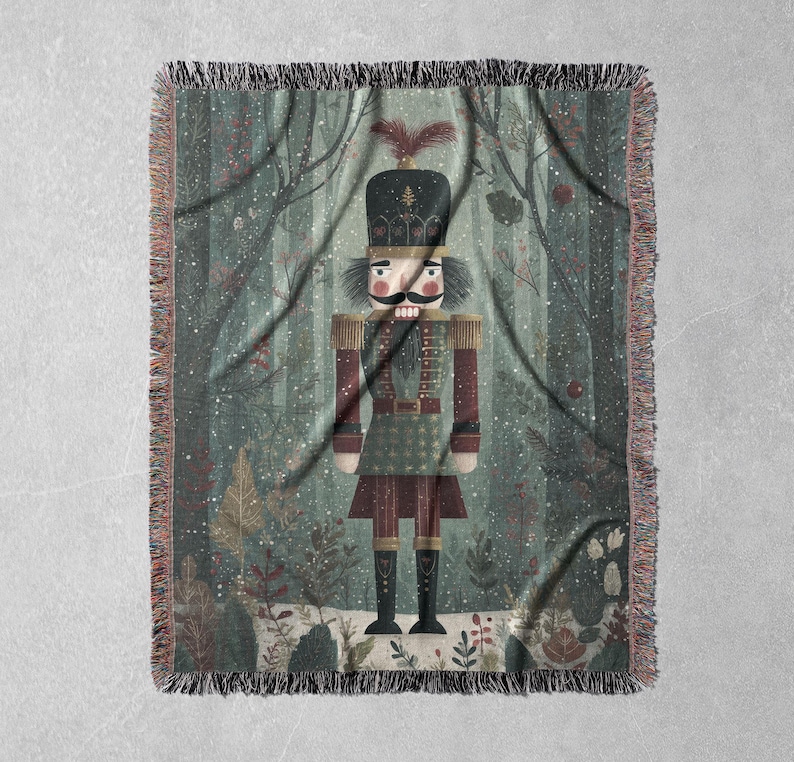 May include: A woven throw blanket featuring a whimsical illustration of a nutcracker soldier in a forest setting. The design includes a detailed nutcracker figure in a uniform, set against a backdrop of trees and falling snow. The blanket has a fringed edge.