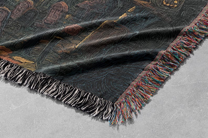 May include: A woven throw blanket with a dark background and a colorful, artistic design. The blanket has a fringed edge with a mix of colors, including red, orange, and blue. The design appears to be a painting.