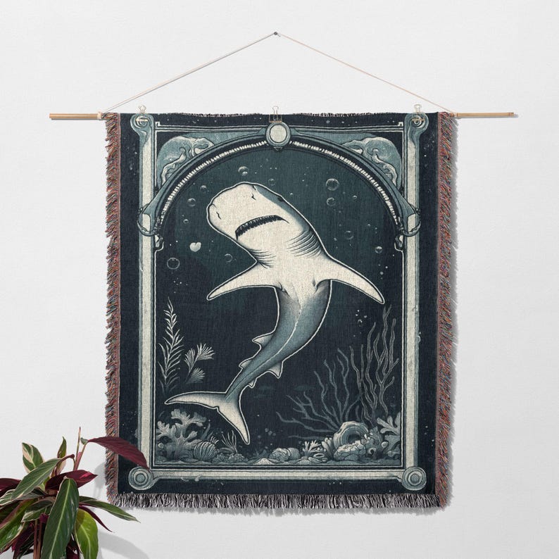 May include: A woven wall tapestry featuring a white shark swimming in a dark blue ocean scene. The shark is depicted in a vintage style with intricate details. The tapestry has a dark blue background with a light blue border.