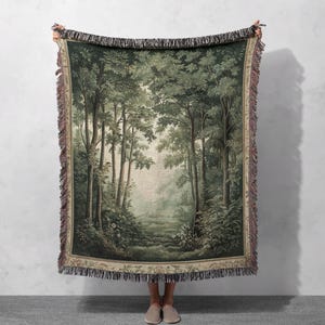 Puede incluir: Una manta de tejido de tapiz que presenta una escena de bosque con un camino que conduce hacia el bosque. El tapiz es verde, marrón y beige con un diseño detallado.