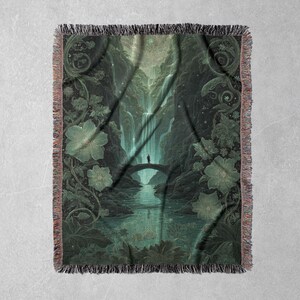 May include: A woven throw blanket featuring a detailed illustration of a serene landscape with a waterfall, bridge, and person. The color palette is dominated by shades of green and teal, with floral and foliage elements. The blanket has a fringed edge.