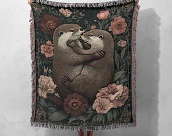 Adorable couverture tissée en coton 100 % avec un couple de loutres et un motif floral, idéale pour une décoration intérieure chaleureuse et des cadeaux romantiques, style cottagecore.