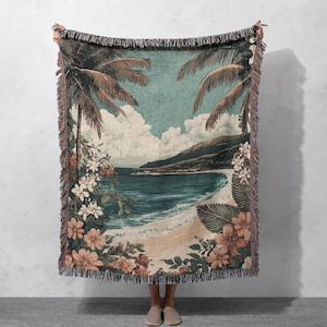 May include: A woven throw blanket with a tropical beach scene. The blanket features palm trees, a sandy beach, blue ocean waves, and lush green foliage. The colors are muted and vintage-inspired.