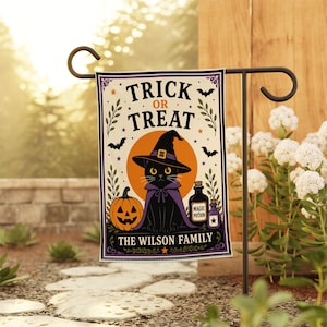 Peut inclure: Un drapeau de jardin rectangulaire illustrant un chat noir portant un chapeau de sorcière et une cape violets, devant une lune orange. Le texte indique "TRICK OR TREAT" et "THE WILSON FAMILY" avec une citrouille et des fioles sur fond crème.