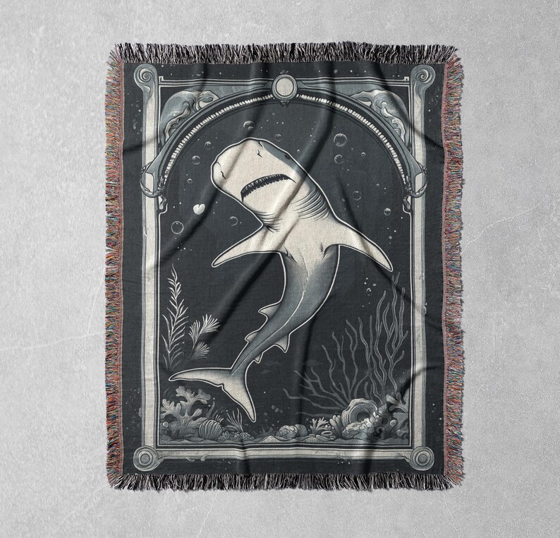May include: A black and white woven tapestry featuring a stylized illustration of a shark swimming in the ocean. The shark is depicted in a vintage style with intricate details. The tapestry has a fringed border.