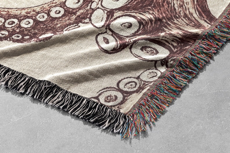 May include: A brown and white woven throw blanket featuring an octopus design. The blanket has a fringe border with multicoloured threads.