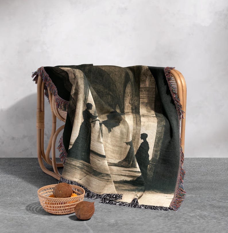 May include: A woven throw blanket with a black and white silhouette design of two figures in a hallway. The blanket has a fringe border and is draped over a wicker chair.