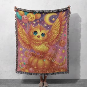 May include: A woven throw blanket featuring a whimsical owl illustration. The owl, with large blue eyes and outstretched wings, is perched on a pumpkin. The background is a starry night sky with Halloween-themed balloons and a crescent moon. The blanket has a fringed edge.