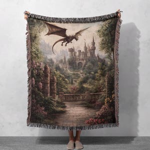 Può includere: Una coperta in tessuto a trama con una scena fantasy con un drago che vola sopra un castello di pietra e alberi verdi lussureggianti. Il castello ha un arco in pietra e un tetto a punta. Il drago è marrone e ha grandi ali.