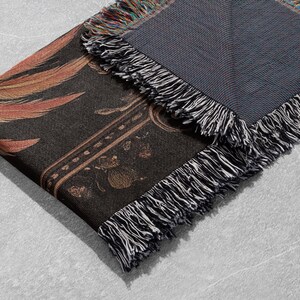 May include: A black and gold woven throw blanket with a fringe border. The blanket features a floral pattern and a geometric design.