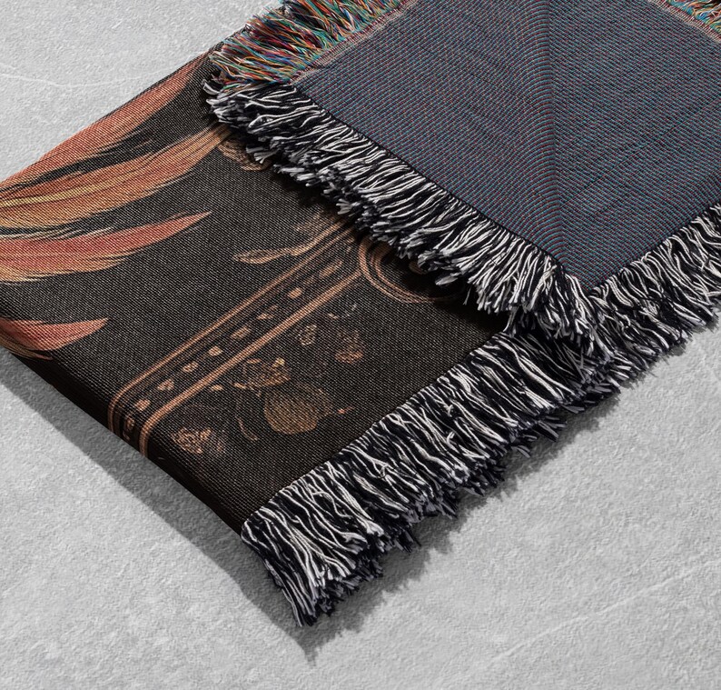 May include: A black and gold woven throw blanket with a fringe border. The blanket features a floral pattern and a geometric design.