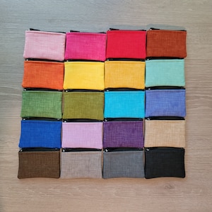 May include: Twenty small zippered pouches in a variety of colors and textures, including pink, red, orange, yellow, green, blue, purple, brown, and gray. The pouches are arranged in a grid pattern on a wooden surface.