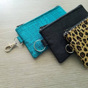 May include: Three zippered pouches with metal rings. The pouches are teal, black, and brown with a leopard print.
