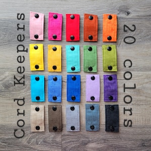 May include: Twenty different colours of cord keepers. The cord keepers are rectangular and made of fabric. They have two black buttons on each side.