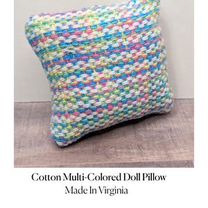 Pode incluir: Uma pequena almofada de boneca de algodão multicolorida. A almofada apresenta um padrão tecido com fios azuis, rosa, amarelos e brancos. O texto "Cotton Multi-Colored Doll Pillow Made In Virginia" está abaixo.