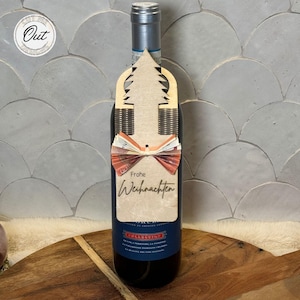 May include: A wooden Christmas tree wine bottle tag with a red bow and the text "Frohe Weihnachten".