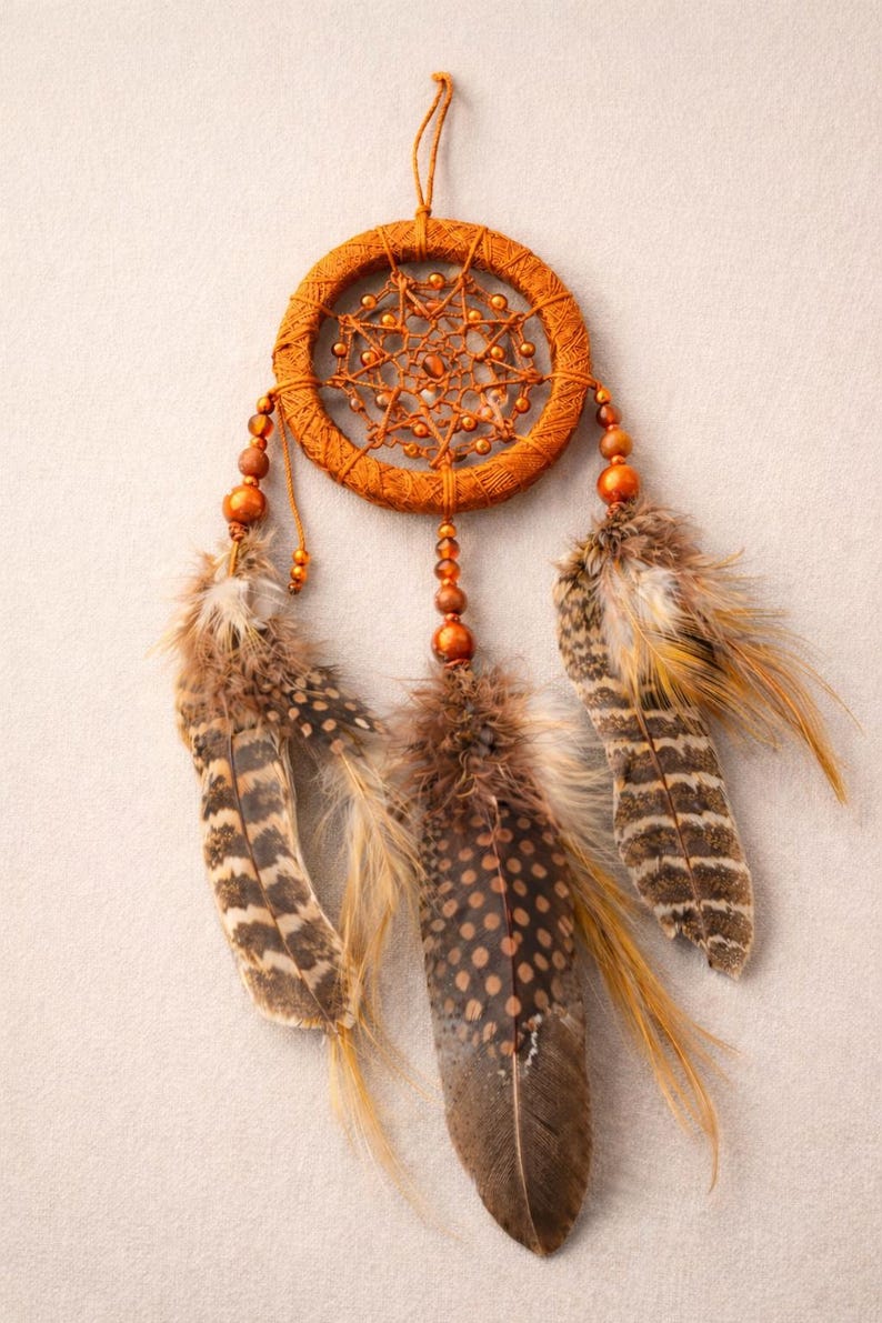 May include: An orange dreamcatcher with a woven circular frame and beaded accents. Three feathers in shades of brown and tan hang below. The dreamcatcher is suspended by a thin orange string.