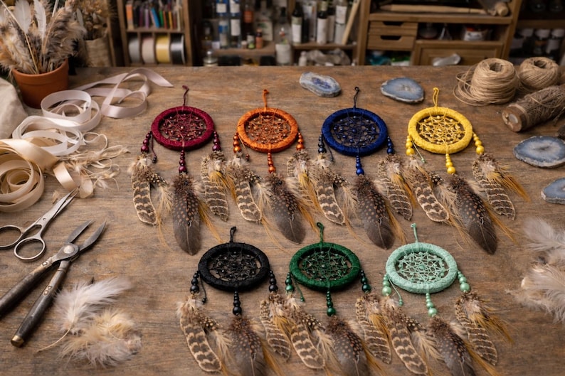 May include: A collection of handmade dream catchers in various colors, including red, orange, blue, yellow, black, green, and turquoise. Each dream catcher features a circular woven web design, adorned with feathers and beads. The dream catchers are displayed on a wooden surface.