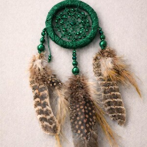 May include: A handcrafted dreamcatcher with a dark green woven hoop, adorned with matching beads and three brown and tan speckled feathers. The dreamcatcher is suspended by a green string, perfect for home decor.