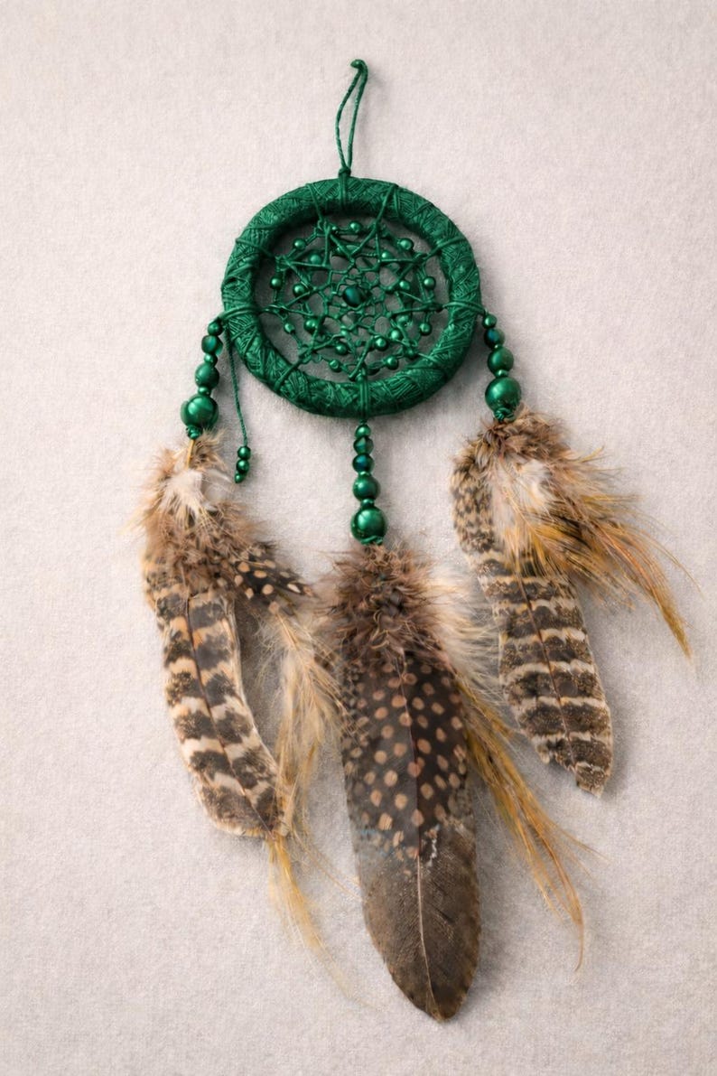 May include: A handcrafted dreamcatcher with a dark green woven hoop, adorned with matching beads and three brown and tan speckled feathers. The dreamcatcher is suspended by a green string, perfect for home decor.