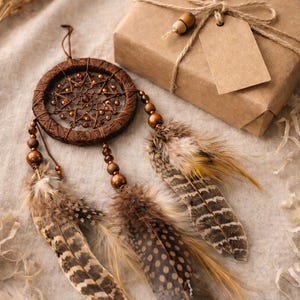 May include: A brown dreamcatcher with feathers and wooden beads, alongside a wrapped gift box tied with twine and a blank tag. The dreamcatcher features a woven center and decorative feathers in shades of brown and tan.