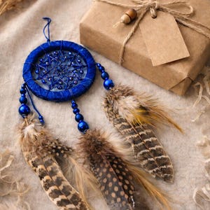 May include: A handcrafted blue dreamcatcher with beaded accents and natural feathers. A wrapped gift box with a tag is also present. The dreamcatcher is a decorative item, often used for home decor.