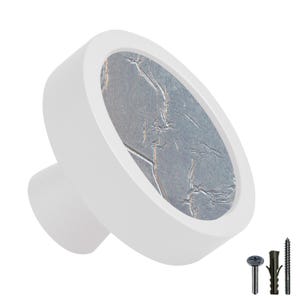 Peut inclure: Bouton de porte rond blanc avec une finition métallisée argentée. Le bouton a un design circulaire surélevé avec une surface texturée.