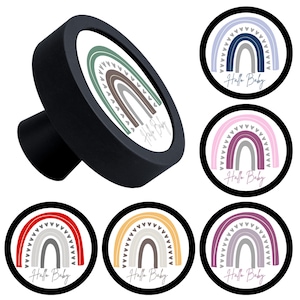 Peut inclure: Un bouton de meuble noir avec un motif arc-en-ciel et le texte "Hallo Baby". Le motif arc-en-ciel présente différentes couleurs, dont le vert, le marron et le gris. D'autres boutons avec des motifs arc-en-ciel de différentes couleurs sont également présentés.