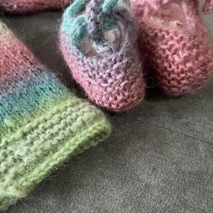 May include: A set of knitted baby booties and a matching hat in a rainbow of colors, including pink, green, blue, and purple.