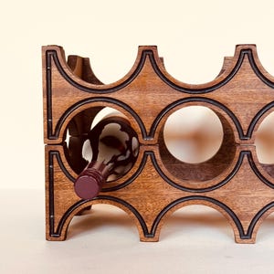 May include: A wooden wine rack with a geometric design. The rack is made of dark brown wood with black accents and holds multiple bottles. One bottle is partially inserted into a circular opening.