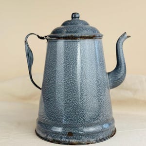 May include: Vintage blue speckled enamelware coffee pot with a lid and handle. The pot has a spout and a rounded body. The enamelware has a speckled pattern and a rustic appearance. The pot is likely made of metal and is a classic kitchenware item.