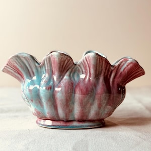 May include: A ceramic bowl with a scalloped rim, featuring a blend of teal and maroon colors. The bowl has a pedestal base and a glossy finish, suitable for decorative use.