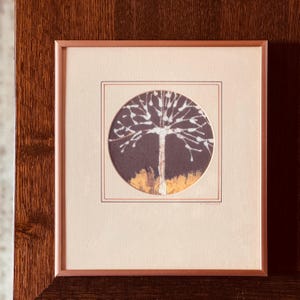 May include: Framed artwork featuring a tree illustration. The tree has white branches and a brown trunk set against a dark background. The artwork is framed in a brown wooden frame with a light beige mat.