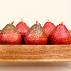 May include: Five pear-shaped decorative objects with a red, crackled finish and dark, weathered tops. Each piece features a small, light-colored stem at the apex. The objects are arranged in a single row inside a rectangular wooden tray.