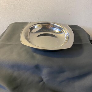 Puede incluir: Un plato de servir cuadrado de plata con un borde ligeramente elevado y una superficie lisa y reflectante.