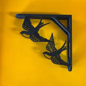 May include: Black metal shelf bracket with a decorative design of two stylized birds in flight.